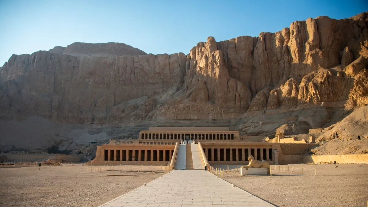 معبد حتشبسوت الجنائزي في الأقصر مع خلفية جبلية صخرية تحت ضوء الشمس في مشهد يعكس التراث الفرعوني والأهمية التاريخية للمدينة.