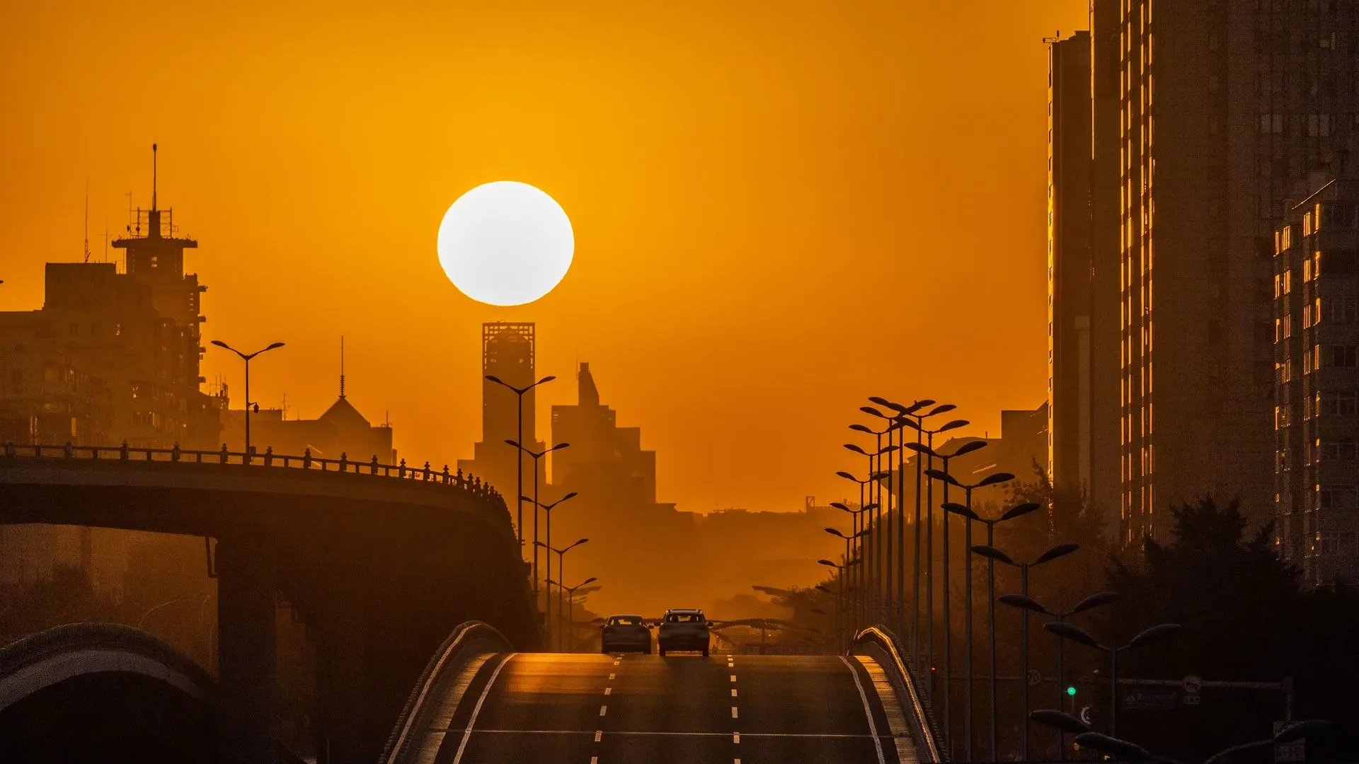 شروق الشمس عند الاعتدال الخريفي في مدينة حضرية مع جسور ومبانٍ، يبرز تأثير الانكسار الجوي على طول النهار.