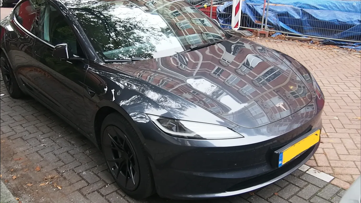 سيارة Tesla Model 3 Highland سوداء مزودة بنظام القيادة الذاتية FSD تقف في شارع أمستردام، تعكس المباني المحيطة على هيكلها اللامع.